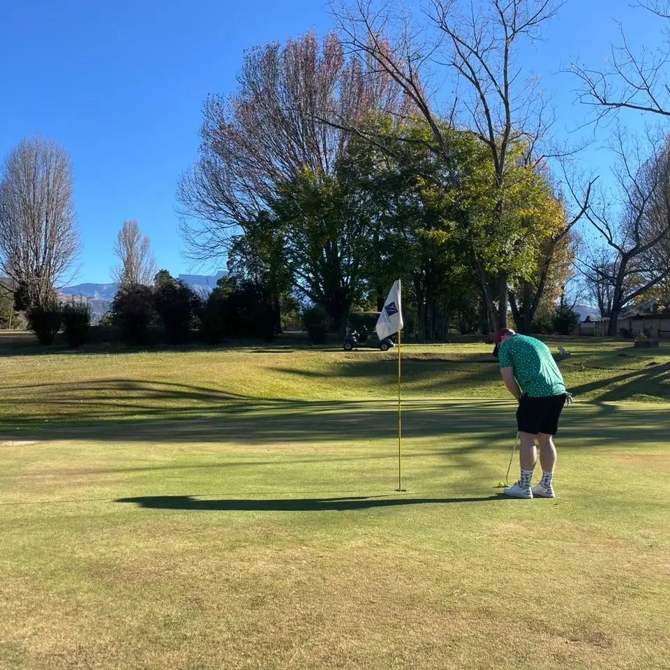 Golfer putting on a green with Drakensberg mountains behind