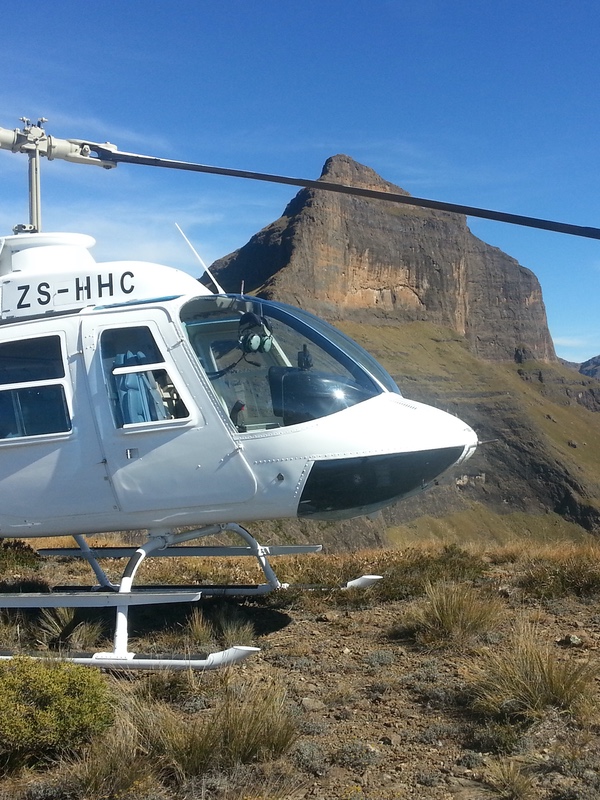 Helicopter on a Drakensberg mountain ledge, peaks behind